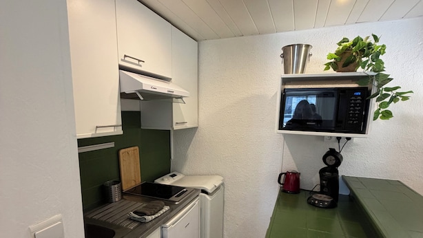 Cocina compacta con armarios blancos, microondas, hervidor y una pequeña encimera.