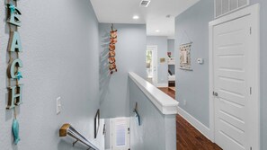 A hallway with a white railing, a door, and a wall-mounted decoration. - 🌴 Little Bird’s Nest | 4BR | Near Beach | Community Pool | 30A 🏖️ (Santa Rosa Beach)