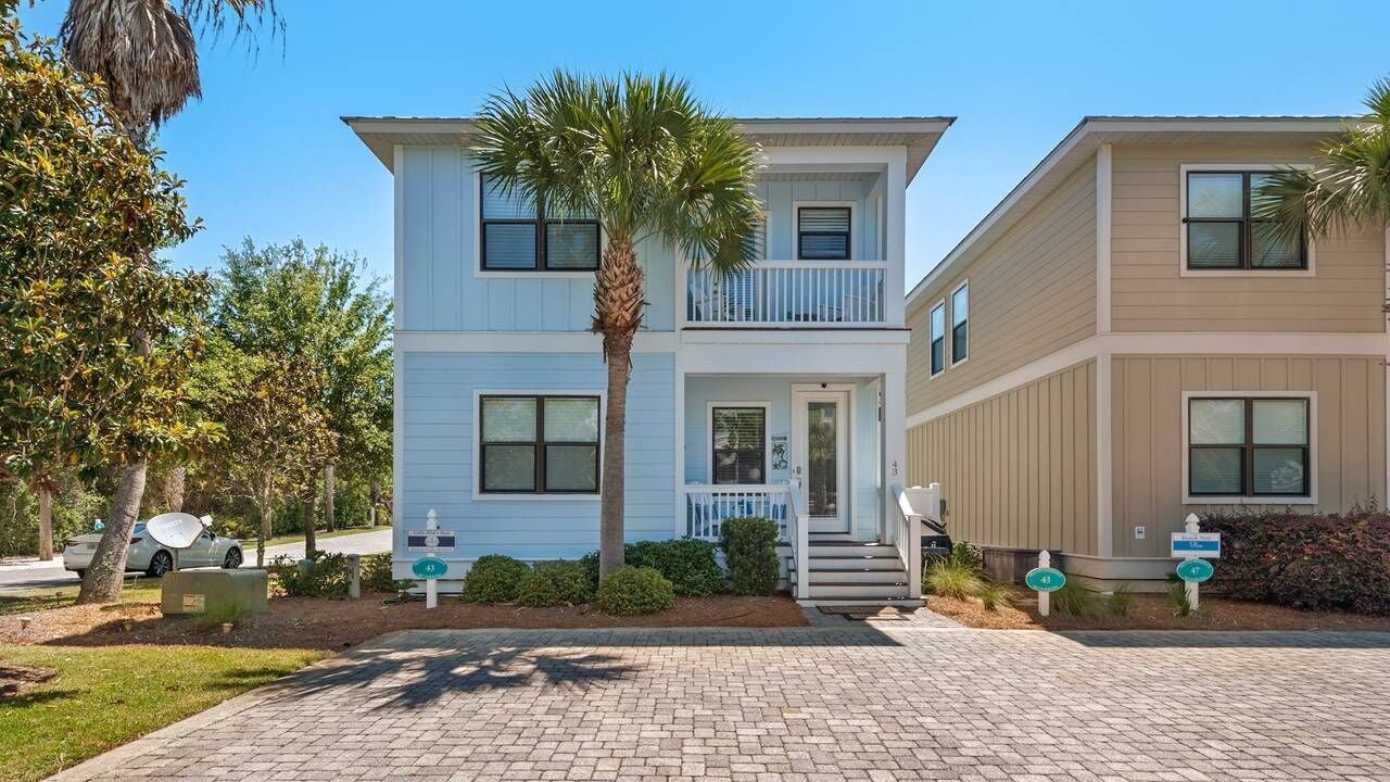 A two-story residential building with a front porch, a palm tree, and a driveway.