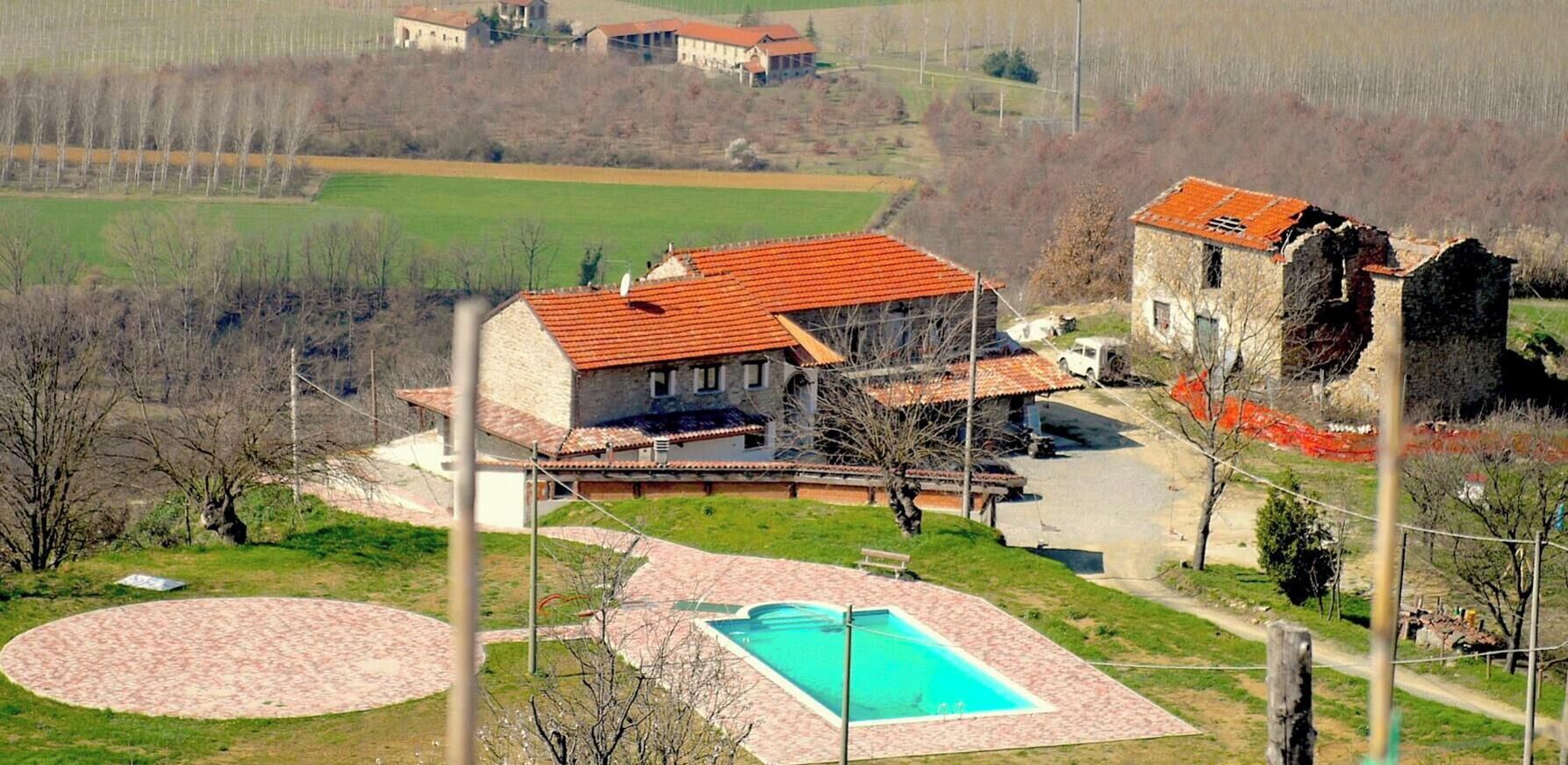 Une grande maison avec une piscine, entourée de champs et d’un petit jardin.