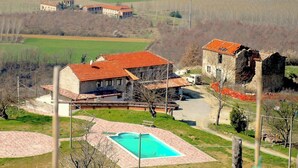 A large house with a swimming pool, surrounded by fields and a small garden.