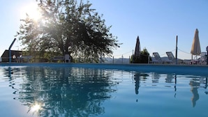 A clear swimming pool with lounge chairs and umbrellas, surrounded by trees and a clear sky. - Casale Trusella (Piemonte)