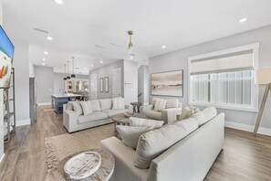 A modern living room with a sectional sofa, a coffee table, and a large window with blinds. - The Lookout | Rooftop Hot Tub | 4 Bikes | Community Pool! (Inlet Beach)