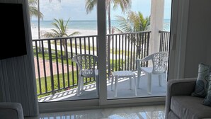 Ein Zimmer mit Balkon und Blick auf einen Strand, möbliert mit einer Couch, Stühlen und einem Couchtisch.