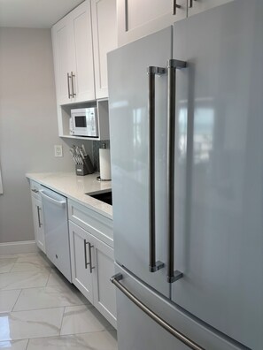 A modern kitchen with white cabinetry, a stainless steel refrigerator, a microwave, and a dishwasher. - The Shores Condos - BEST in the Building!  TRUE Beachfront - End Unit! (Fort Myers Beach)