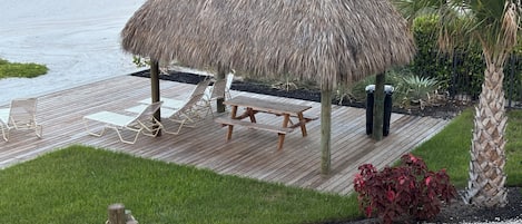 Une terrasse au bord de la plage, agrémentée d’un gazebo à toit de chaume, de chaises longues et d’une table de pique-nique.