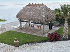 Une terrasse au bord de la plage, agrémentée d’un gazebo à toit de chaume, de chaises longues et d’une table de pique-nique.