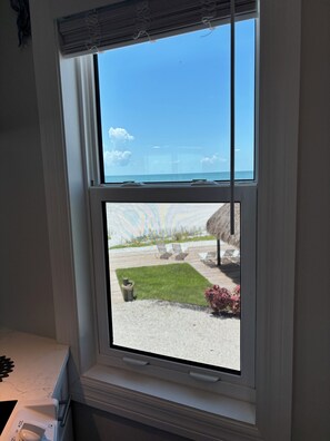 A window with a view of a grassy area and a building across the water. - The Shores Condos - BEST in the Building!  TRUE Beachfront - End Unit! (Fort Myers Beach)