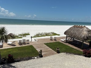 A beachside resort with a wooden deck, lounge chairs, a thatched-roof pavilion, and a view of the ocean. - The Shores Condos - BEST in the Building!  TRUE Beachfront - End Unit! (Fort Myers Beach)