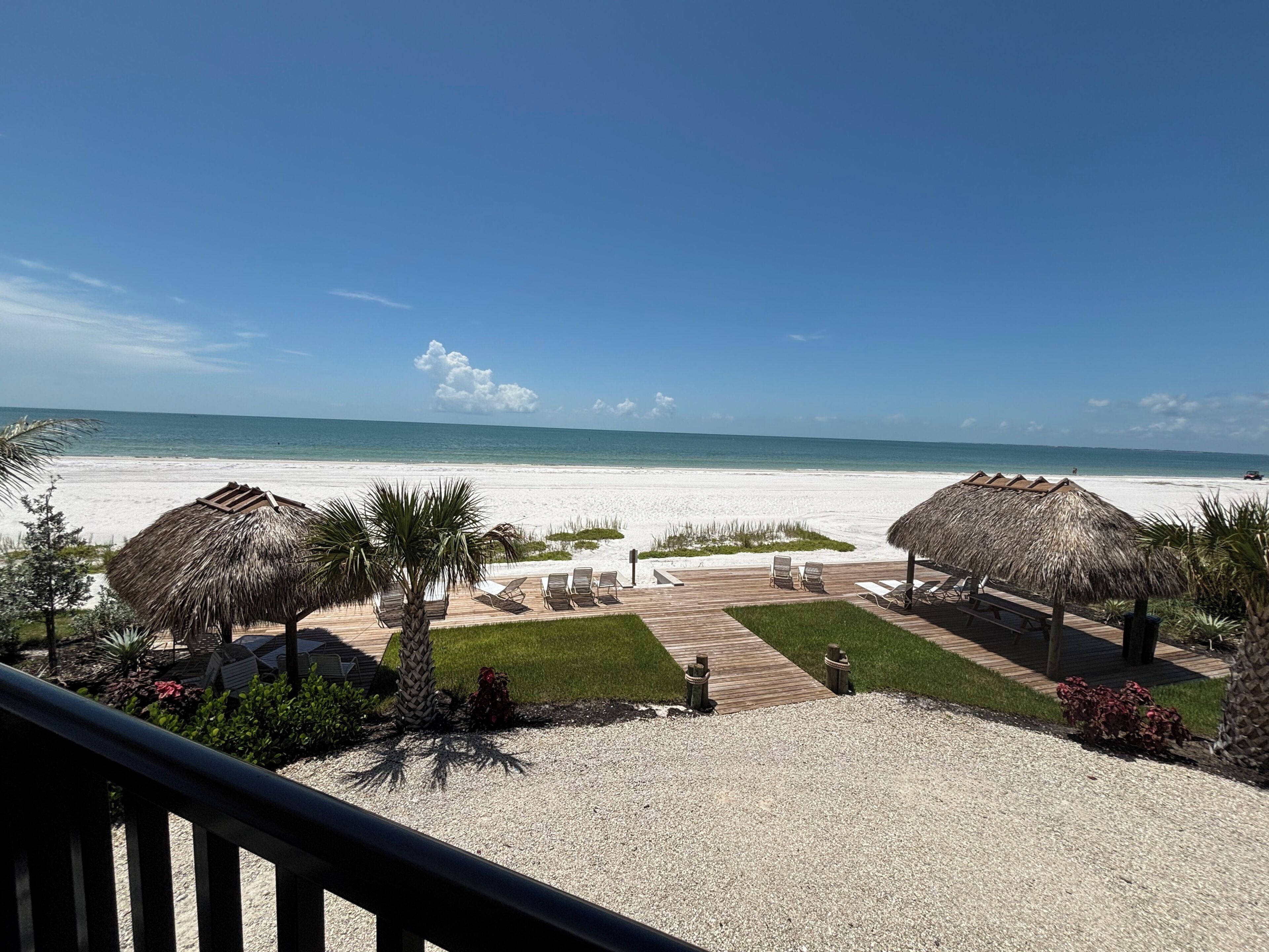 A beach view with a wooden deck, lounge chairs, and thatched umbrellas.