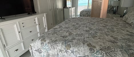 Een slaapkamer met een bed, een televisie, een dressoir en uitzicht op het strand.