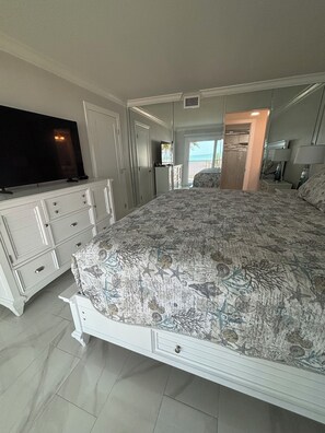 A bedroom with a bed, a TV, a dresser, and a view of the beach. - The Shores Condos - BEST in the Building!  TRUE Beachfront - End Unit! (Fort Myers Beach)