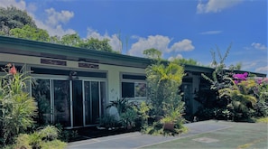 A residential building with a covered porch, surrounded by lush greenery and flowering plants. - Cozy unique 2-bedroom townhome in THE HILLS  of San Isidro de GRECIA (SAN ISIDRO de Grecia)