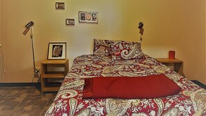 Een slaapkamer met een bed, twee nachtkastjes, een vloerlamp en ingelijste foto's aan de muur.