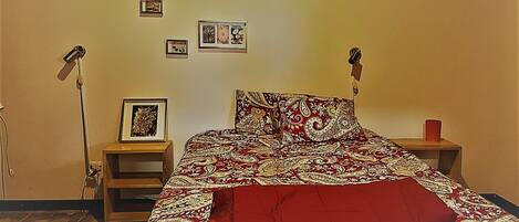 Une chambre à coucher avec un lit, deux tables de chevet, une lampe sur pied et des tableaux encadrés accrochés au mur.