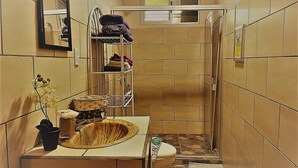 Een smalle badkamer met betegelde wanden, een wastafel, een spiegel en een plank met handdoeken en toiletartikelen.