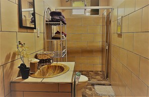 A narrow bathroom with tiled walls, a sink with a basin, a mirror, and a shelf with towels and toiletries. - Cozy unique 2-bedroom townhome in THE HILLS  of San Isidro de GRECIA (SAN ISIDRO de Grecia)