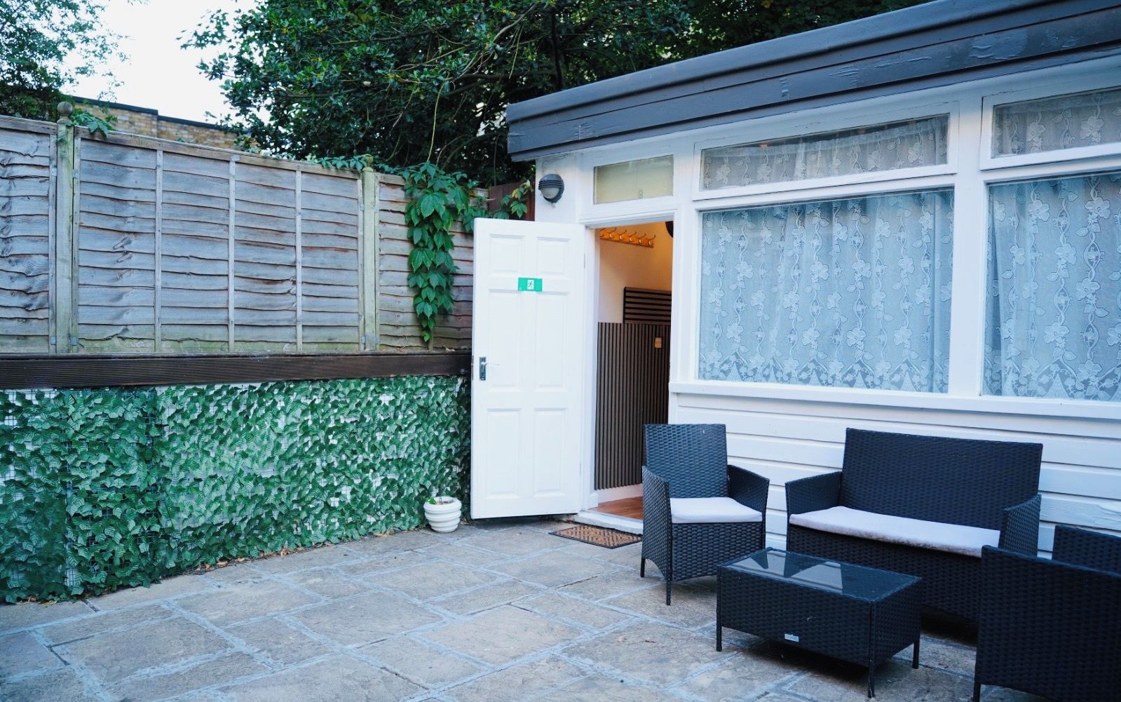 Un espace patio avec une porte blanche, des meubles en osier et un mur recouvert de lierre vert.