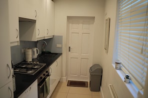 A compact kitchen with white cabinets, a gas stove, a sink, and a trash bin. - Camden,Euston,kingcross Family Apartment (London)