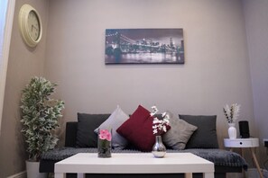 A living room with a sofa, a coffee table, a clock, a framed cityscape picture, and a plant. - Camden,Euston,kingcross Family Apartment (London)