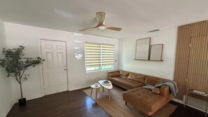 Ein Wohnzimmer mit einem braunen Ledersofa, einem kleinen weißen Tisch, einer Topfpflanze und einem Deckenventilator.