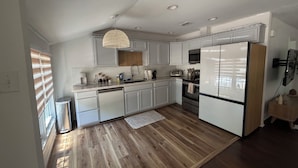 Eine moderne Küche mit weißen Schränken, einem Edelstahl-Kühlschrank, einem eingebauten Backofen und einer Pendelleuchte.