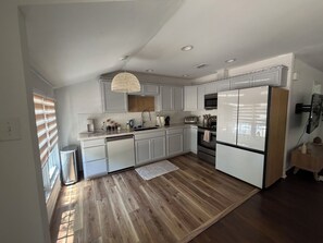 A modern kitchen with white cabinetry, a stainless steel refrigerator, a built-in oven, and a hanging light fixture. - Bright & Peaceful 3-bedroom house with AC in Westworth Village (Westworth Village)
