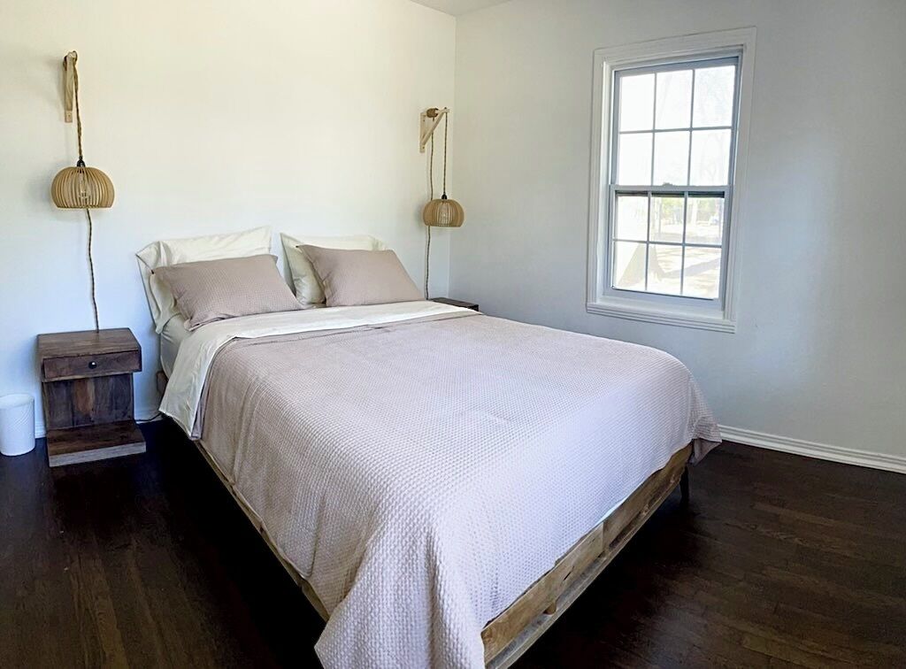 A bedroom with a bed, bedside tables, a window, and a hanging light fixture.