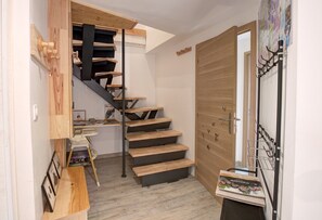 A narrow hallway with a wooden staircase leading to a door with a metal handle.