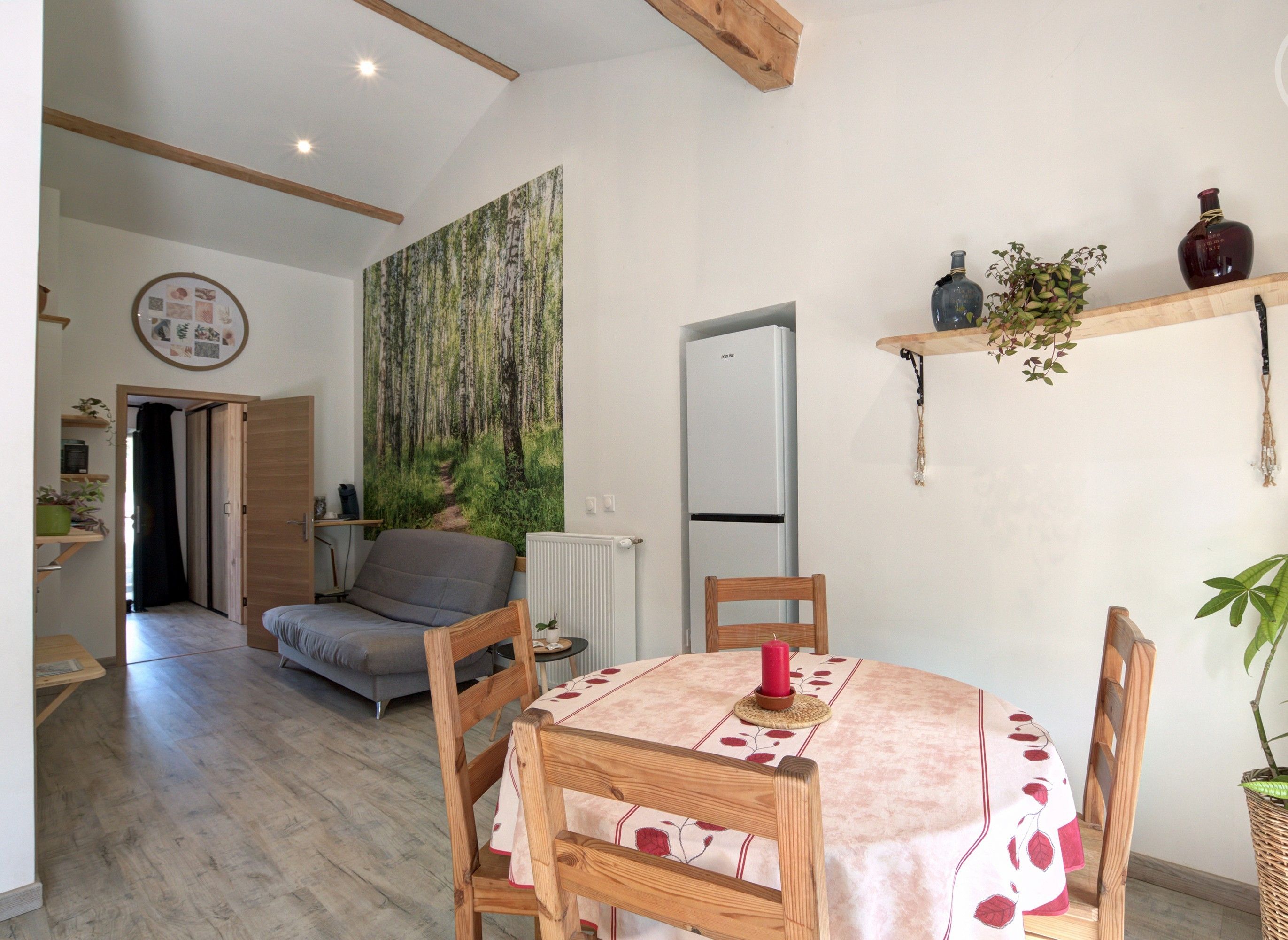 Un salon chaleureux avec une table à manger, des chaises, un canapé et une grande fresque murale sur le thème de la forêt.