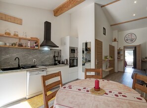 A modern kitchen with white cabinetry, a black range hood, and a dining area with a table set for two.