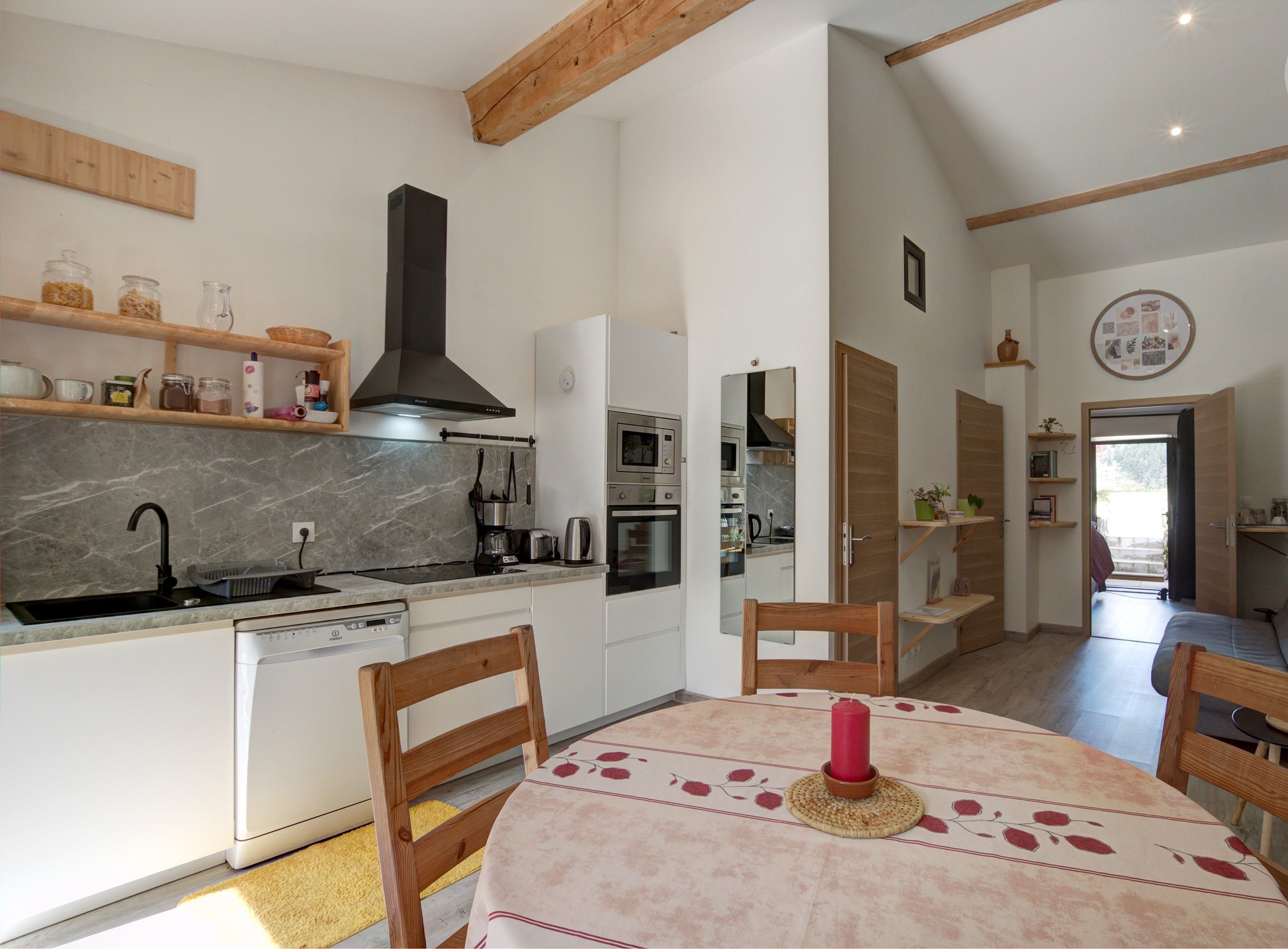 Une cuisine moderne avec des meubles blancs, une hotte noire et un coin repas avec une table dressée pour deux personnes.