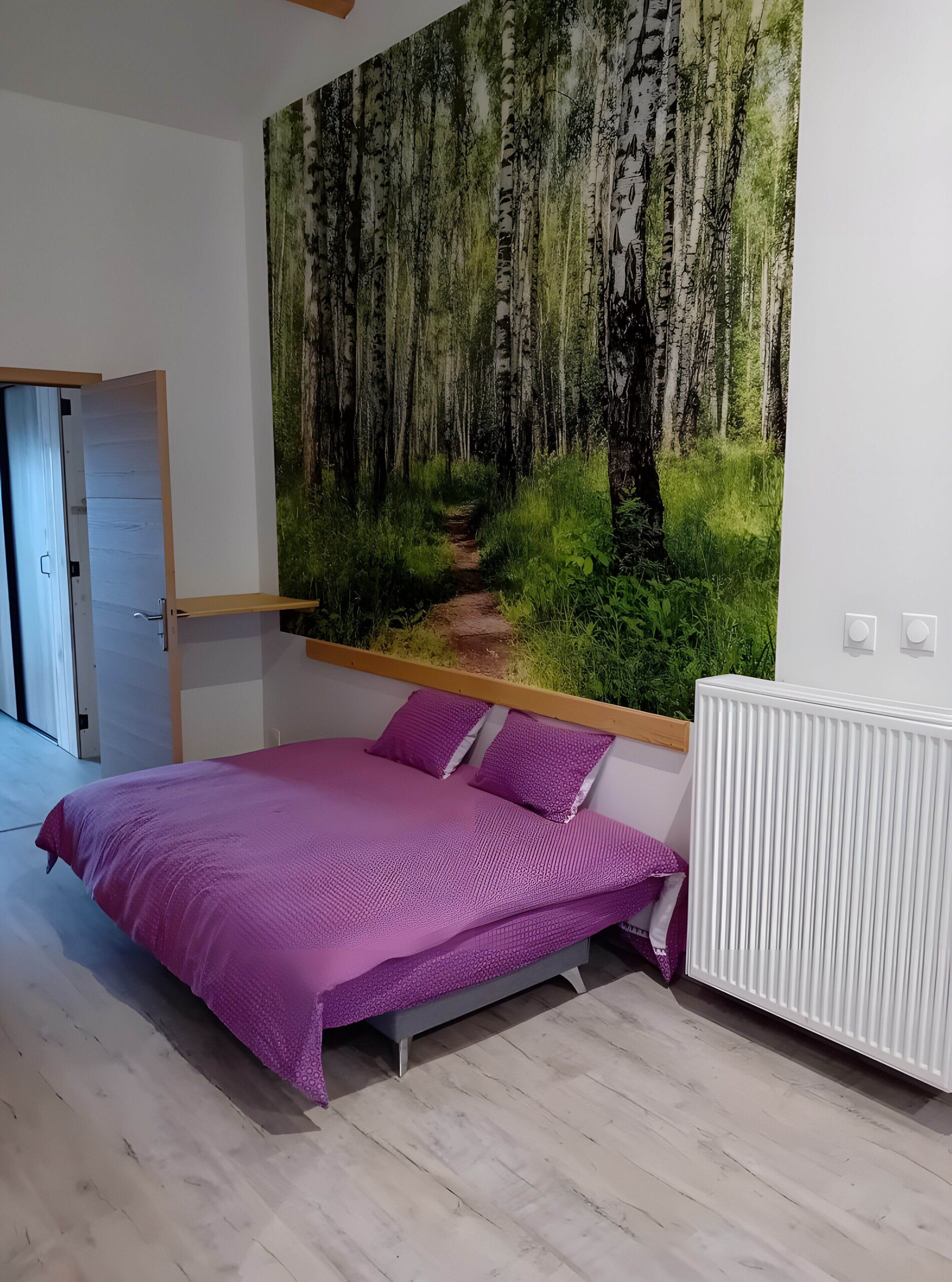 Une chambre à coucher avec un lit, une étagère fixée au mur et une grande fresque représentant une forêt.