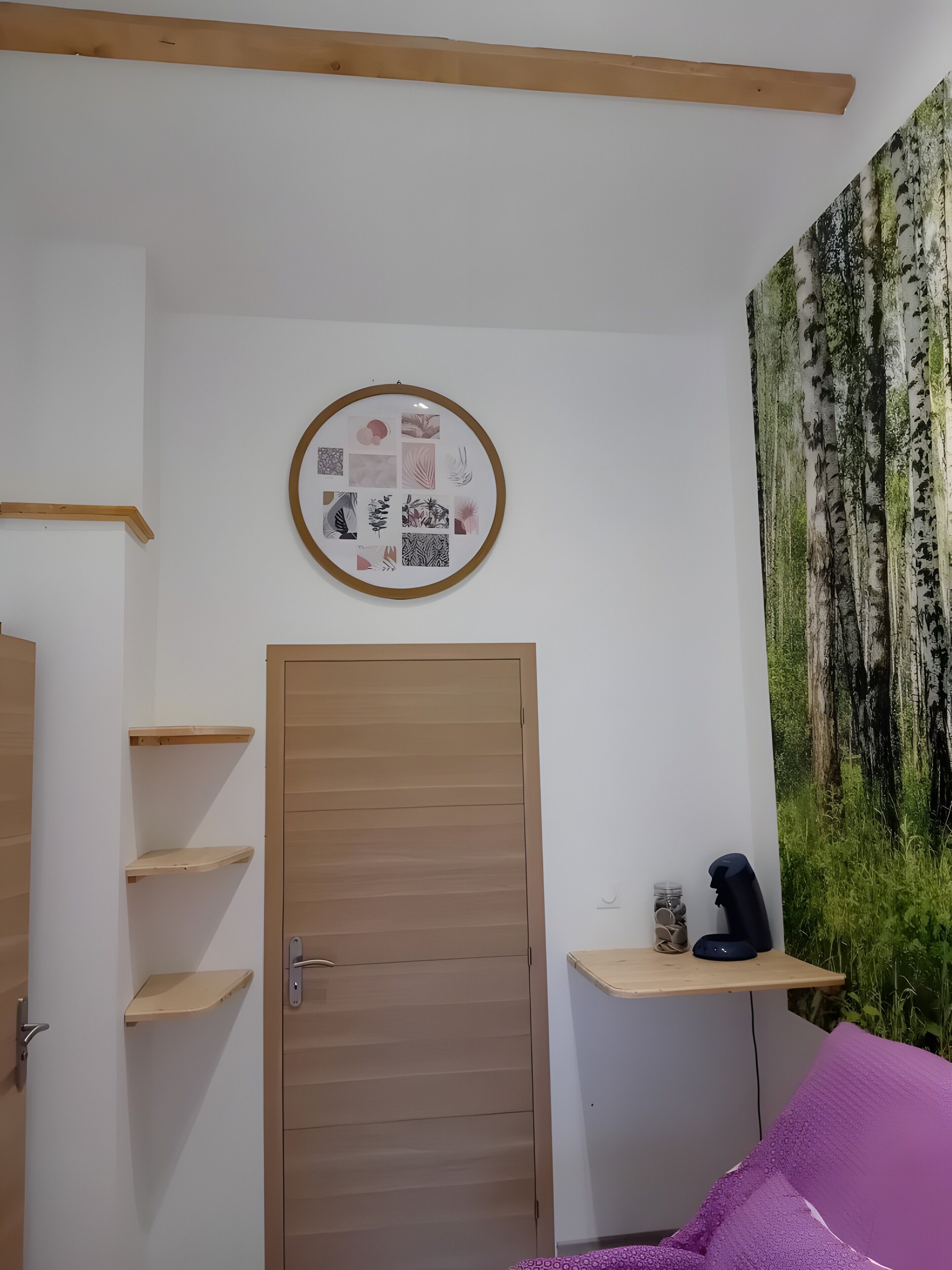 Une pièce avec une porte en bois, une étagère fixée au mur, un tableau encadré et une grande tapisserie représentant une forêt.