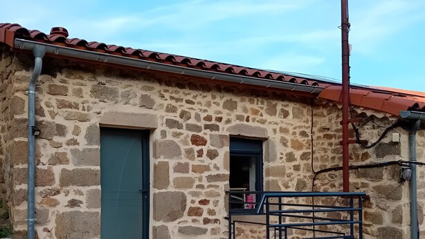 Edifício de pedra com deck de madeira, guarda-corpo de metal e uma porta.
