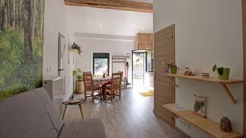 Un salon moderne avec un canapé gris, une table à manger en bois et des chaises. Une grande fenêtre offre une vue sur la verdure à l’extérieur.