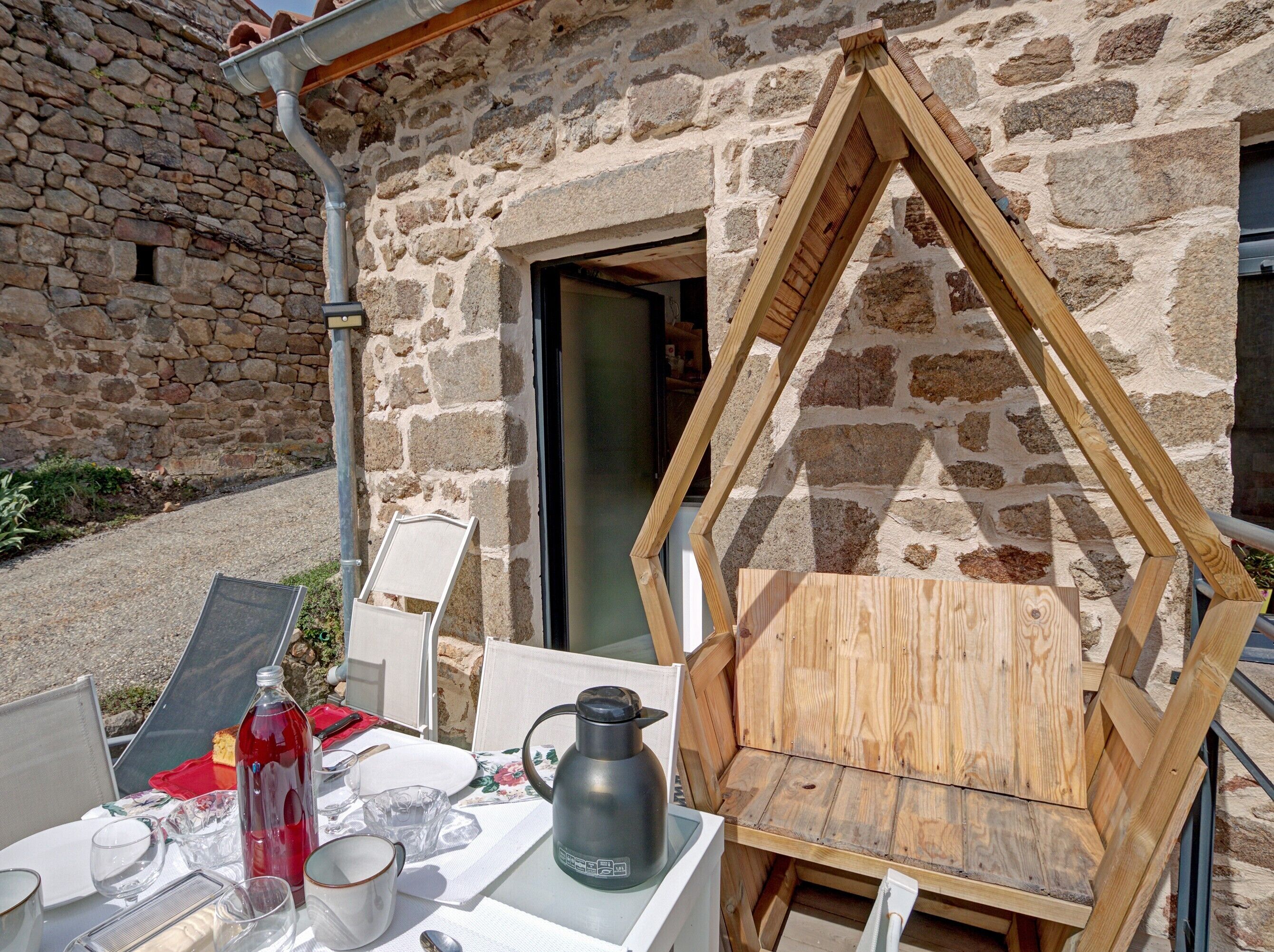 Un bâtiment en pierre avec une table et des chaises en bois disposées à l’extérieur.