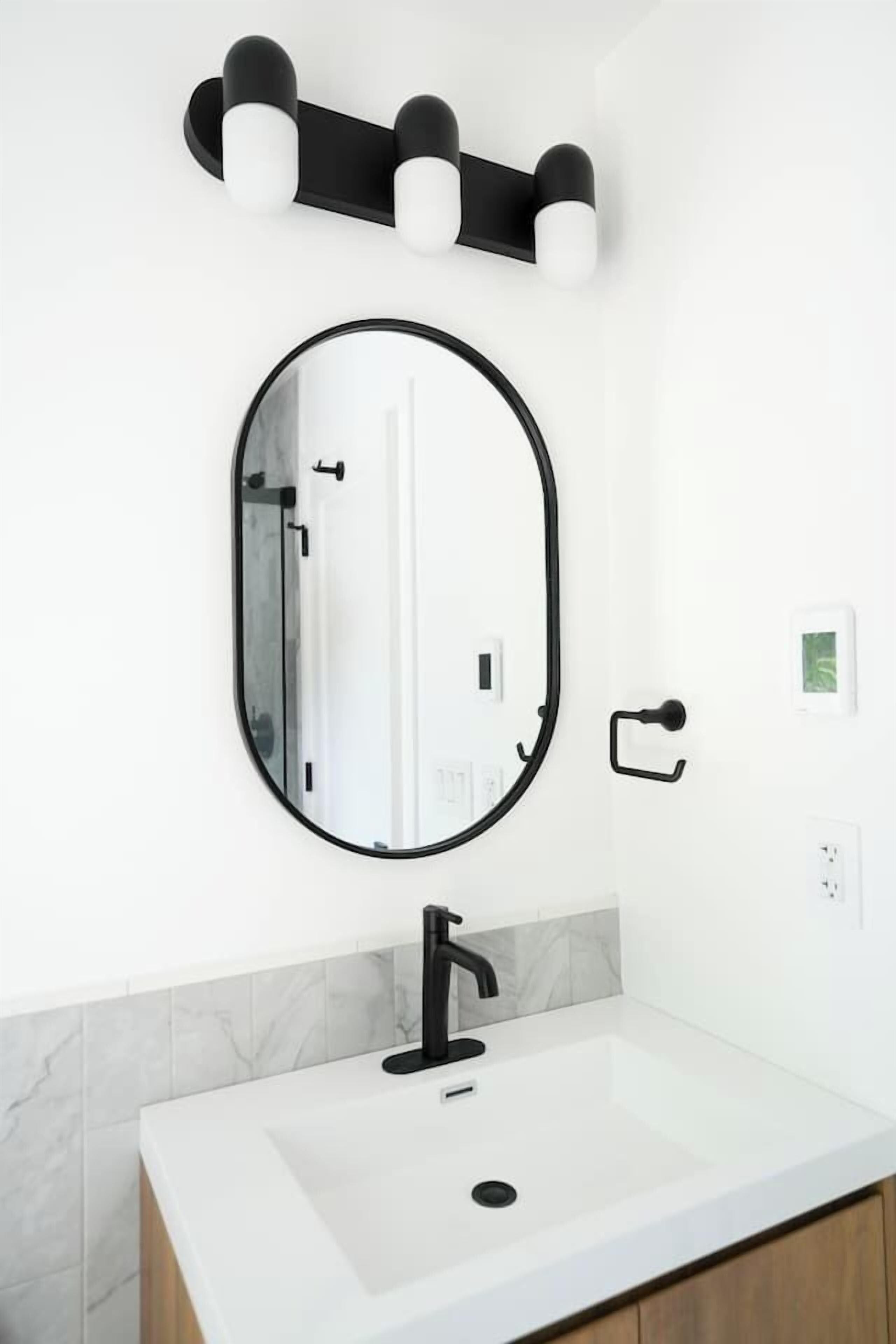 Een badkamer met een witte wastafel, een zwarte kraan en een ronde spiegel met een zwarte lijst.