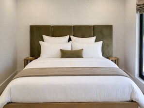 Una cama con cabecera, ropa de cama blanca y una manta marrón.