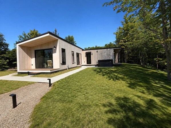 Una casa moderna con un amplio ventanal, un patio de hormigón y un césped cuidado.