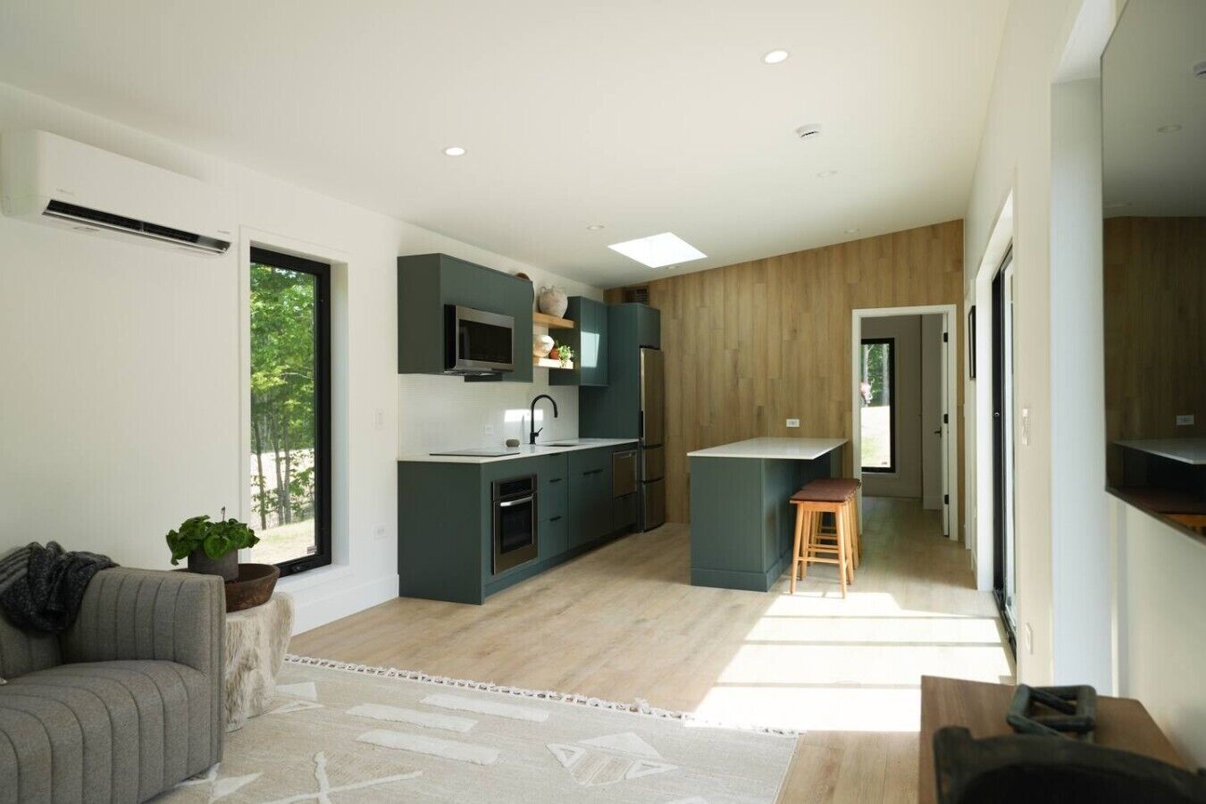 Una cocina moderna con electrodomésticos integrados, una zona de comedor con un taburete de bar y una sala de estar con un sofá y una planta.