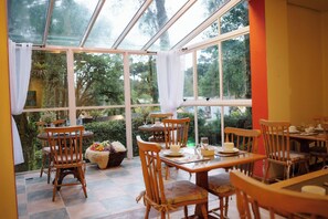 A conservatory with wooden furniture, glass doors, and a view of greenery. - Pousada Pinhão e Poesia (Canela)