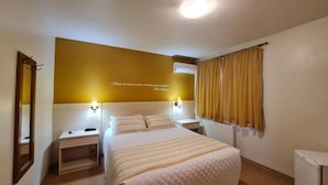 Quarto de hotel com cama, mesas de cabeceira, espelho, ar condicionado fixado na parede e janela com cortinas.