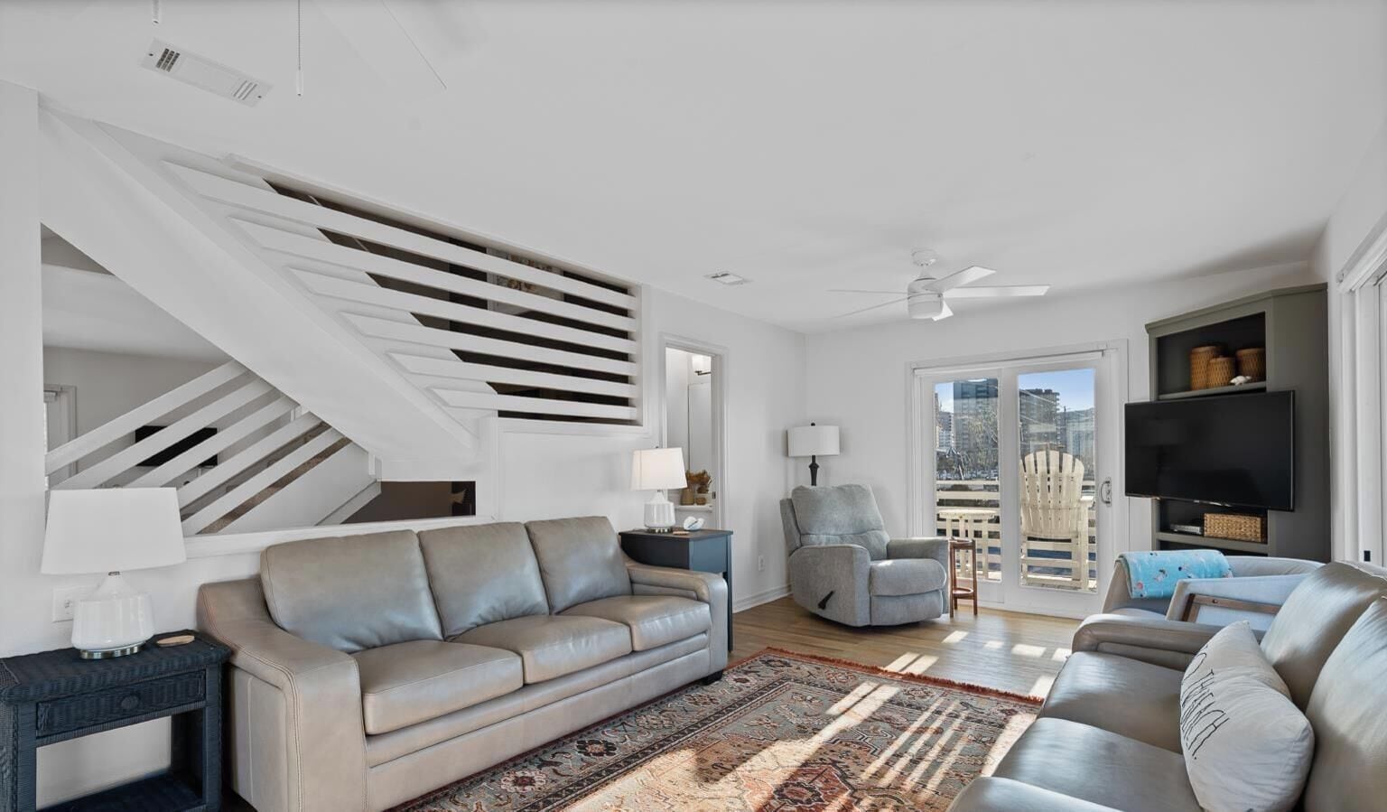 Ein modernes Wohnzimmer mit Treppe, einem grauen Sofa, einem Sessel, einem Fernseher und einem Balkon mit Blick.