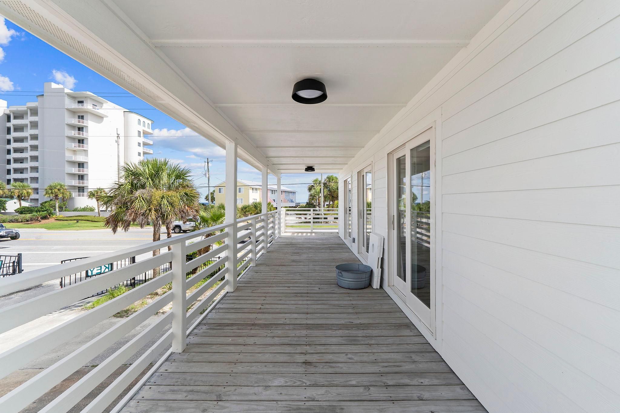 A covered wooden deck with a railing, a single light fixture, and a view of the street and buildings in the background.