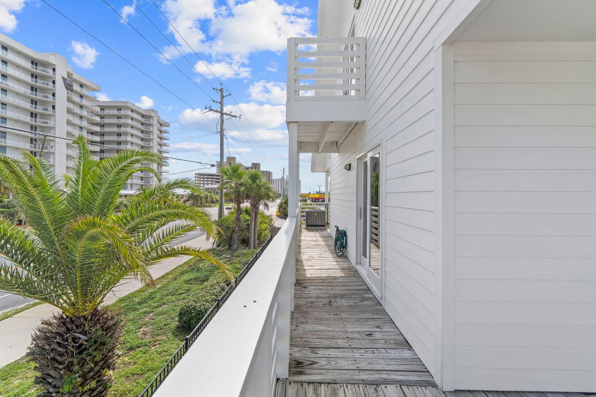 A balcony with a wooden floor, overlooking a street with palm trees and a building in the background.