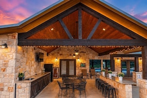 A covered outdoor area with stone walls, a wooden ceiling, a bar area, and seating. - Longhorn Lodge 5BD Pool Near Frio River (Concan)