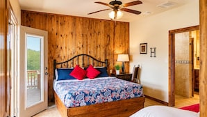 Un dormitorio con cabecera de madera, cama con ropa de cama floral, ventilador de techo y puerta corrediza de vidrio que da a un área exterior.
