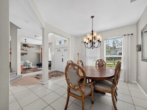 A dining area with a round table and chairs, a chandelier, and a view of the outdoors through a window. - Sunset to Magic 6BR Davenport Home with Private Pool Near Disney (Davenport)