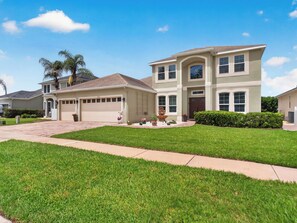 A two-story house with a garage, a well-maintained lawn, and a clear sky. - Sunset to Magic 6BR Davenport Home with Private Pool Near Disney (Davenport)